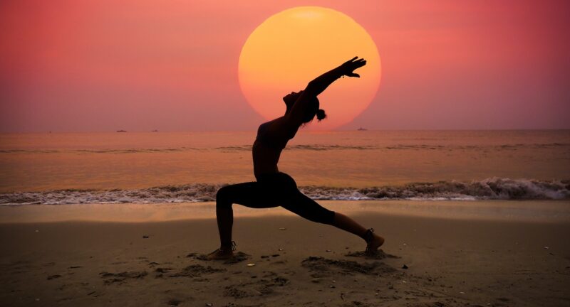 Silhouette young woman practicing yoga on the beach at sunrise